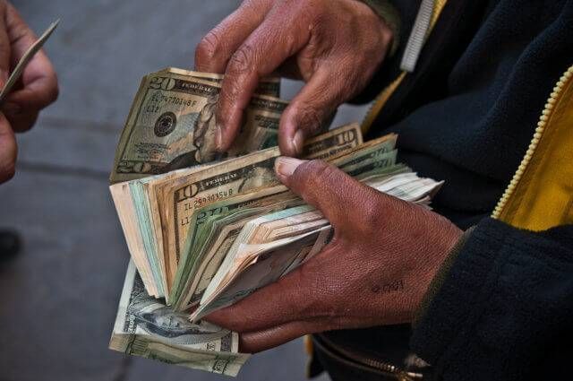 A person holding a large stack of American dollars and rifling through them.