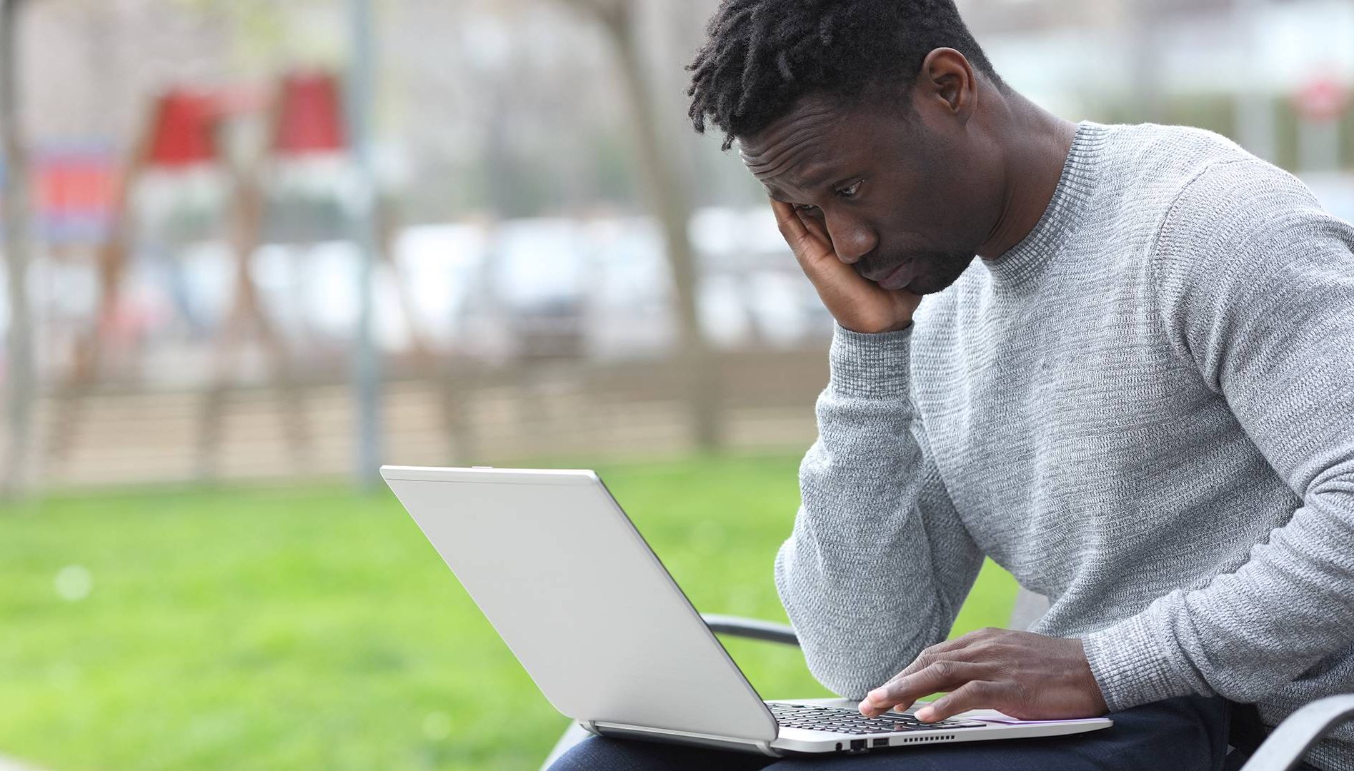 Photo of a worried black man reading bad news on laptop at the park. Rewire PBS Health Vicarious Trauma
