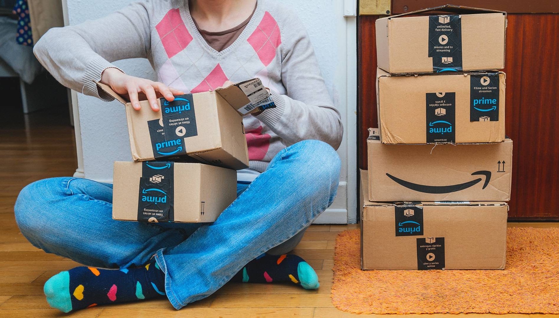 Woman next to stack of Amazon Prime packages delivered to a home door. Rewire PBS Money Money