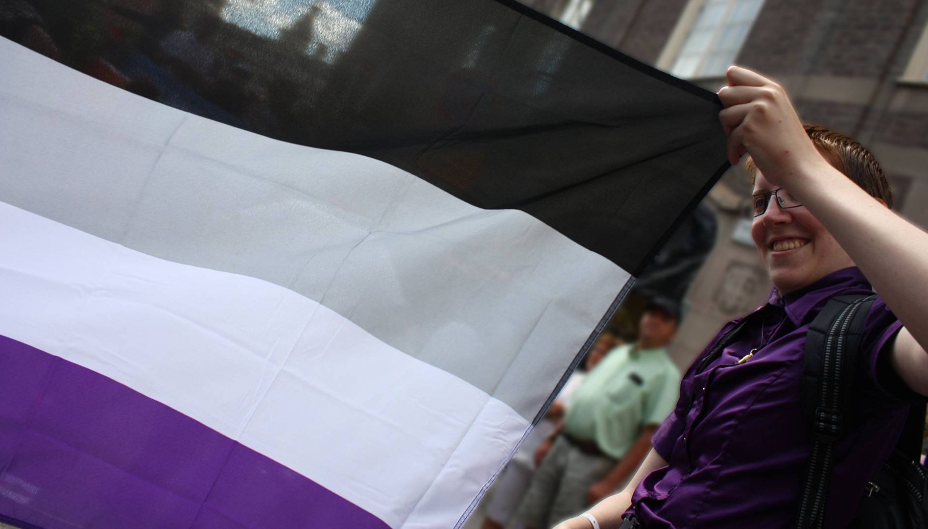 A person holds the edge of an asexual pride flag. Rewire PBS Love Asexual