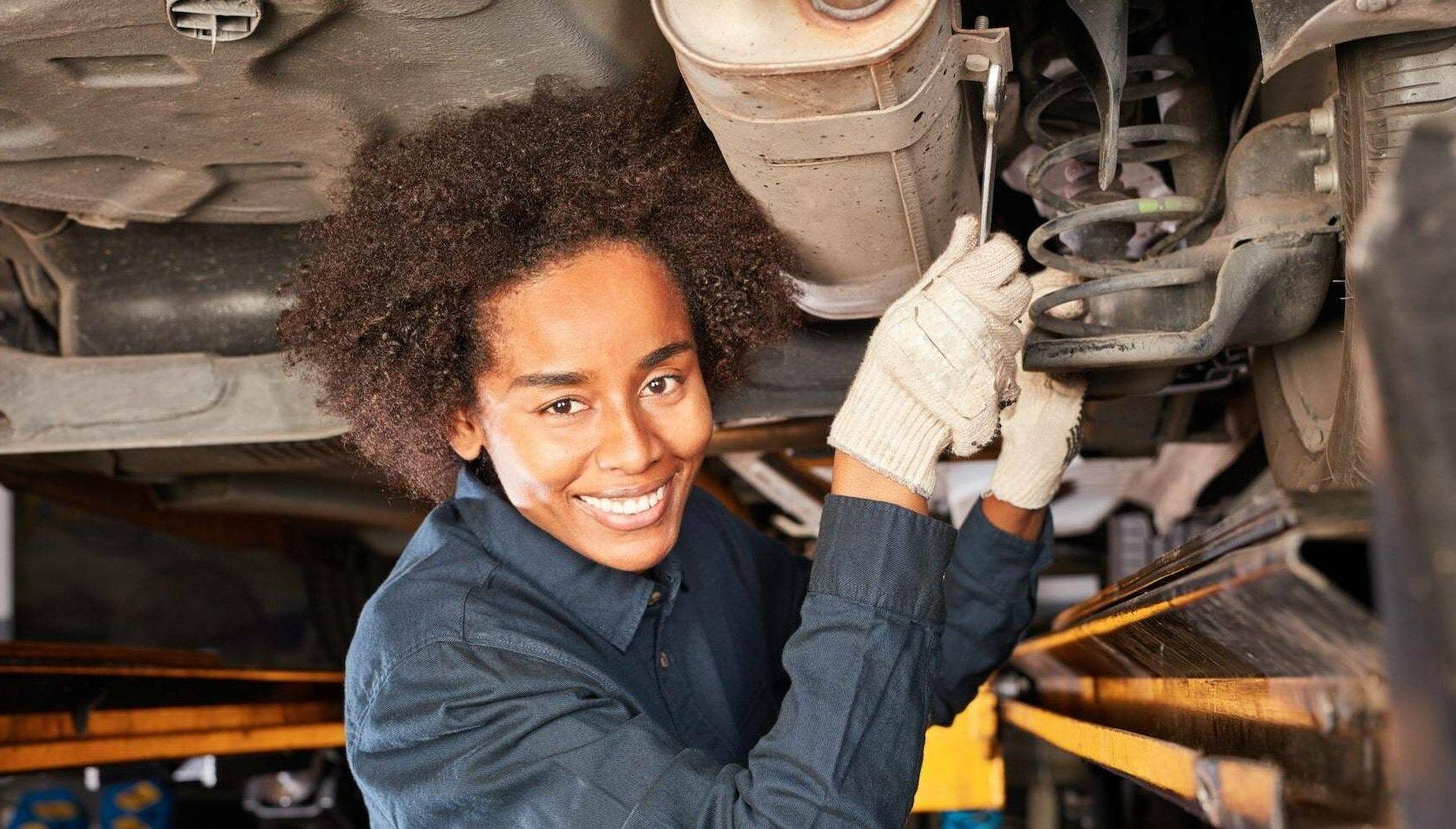 Woman working on the underside of an automobile. Rewire PBS Work Auto Industry