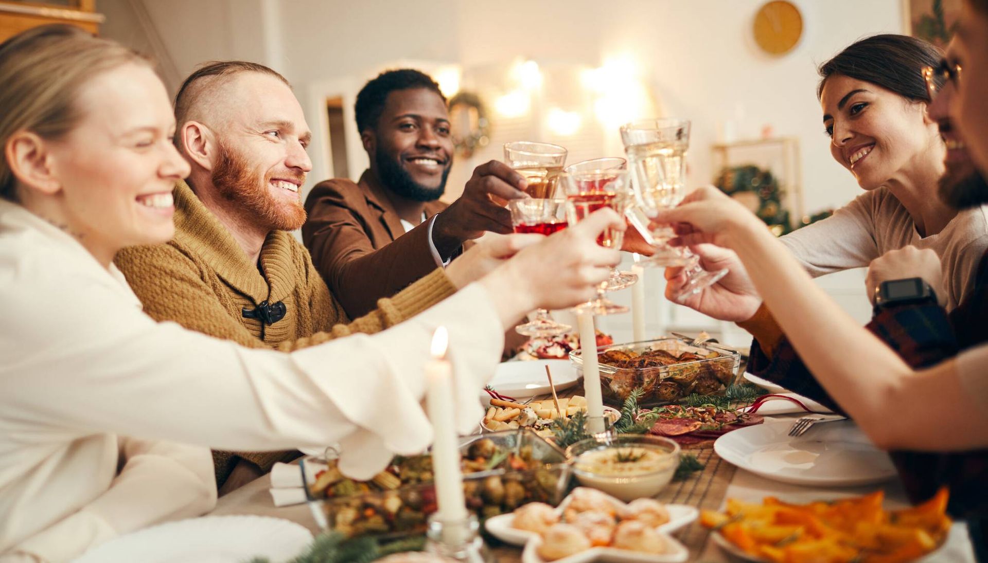 Multi-ethnic group of people raising glasses sitting at beautiful dinner table celebrating Christmas with friends and family
