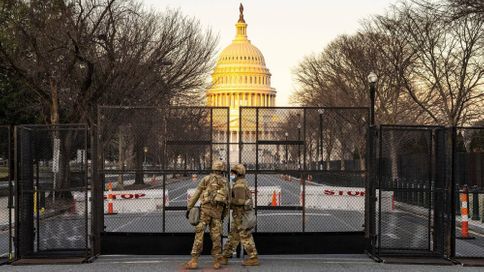 Two National Guard members stand in front of a fence surrounding the U.S. Capitol building in Washington, D.C.