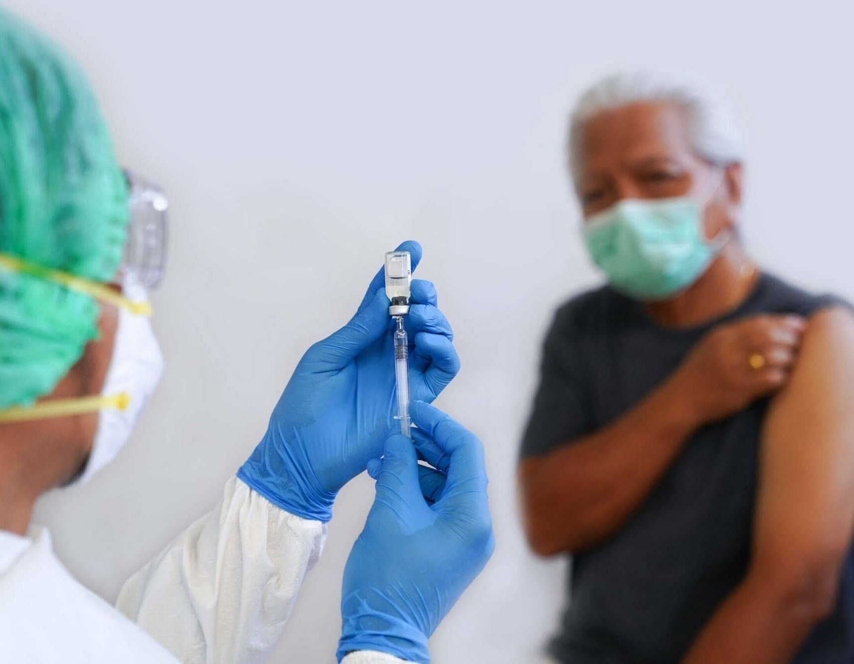 Photograph of a medical worker preparing a COVID vaccination shot for an older man who is wearing a mask and pulling up his shirt sleeve, Black doctors, COVID vaccine, Rewire