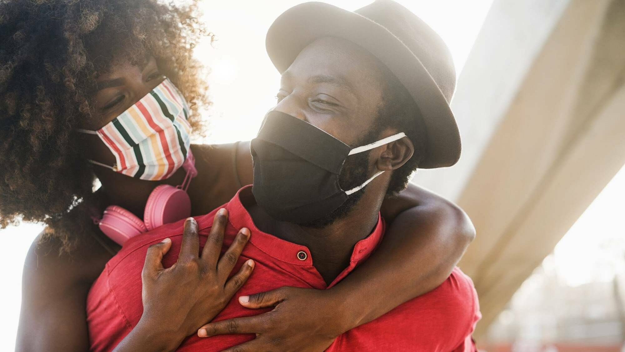Photograph of a couple wearing masks and embracing and looking into each others eyes