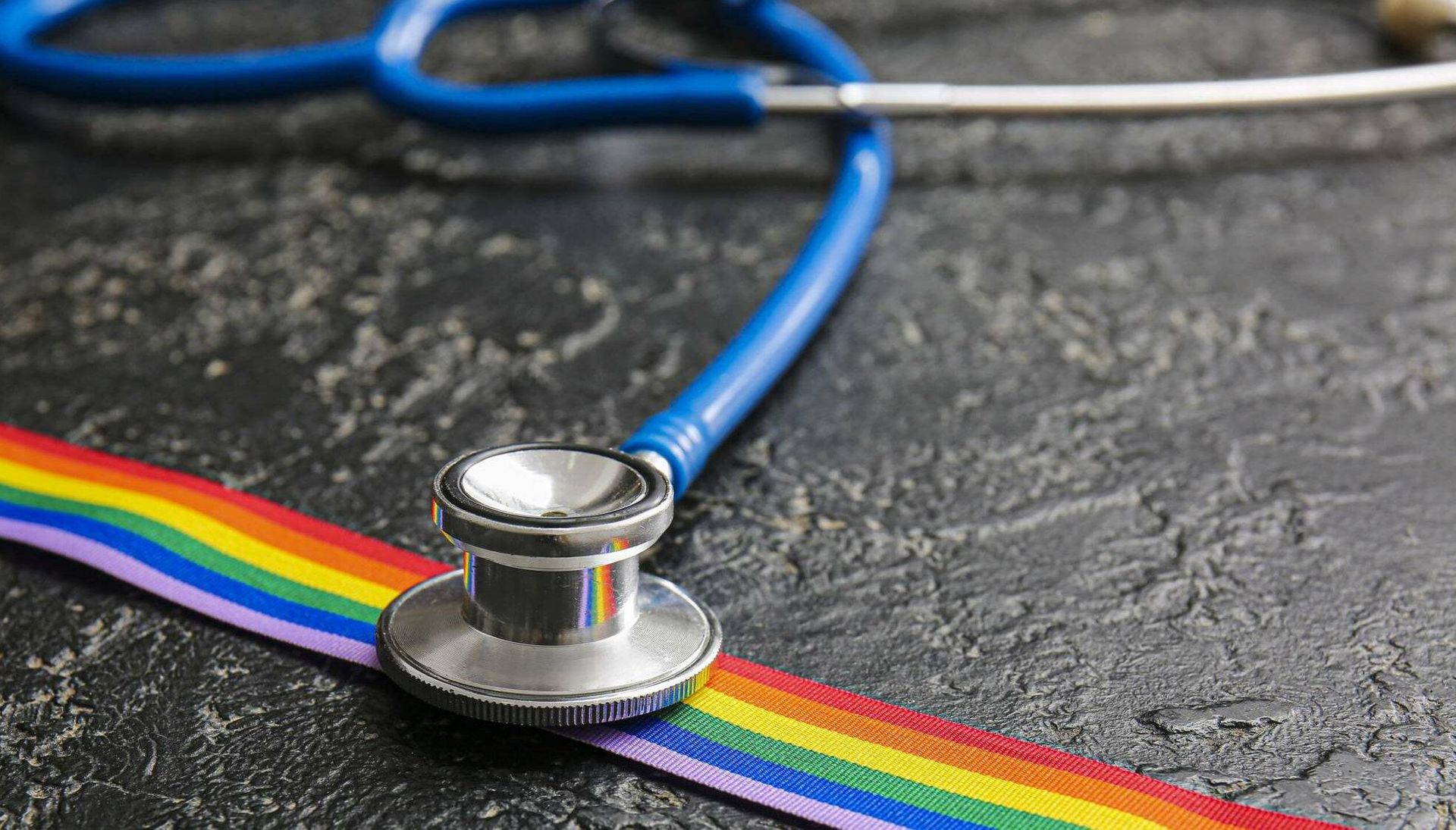 Photograph of stethoscope and rainbow ribbon on dark background