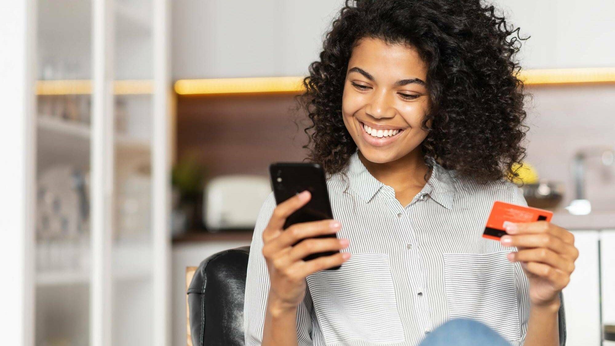 Young black woman holding smart phone and credit card while smiling, LGBTQ, brighter future, new app, inclusive banking