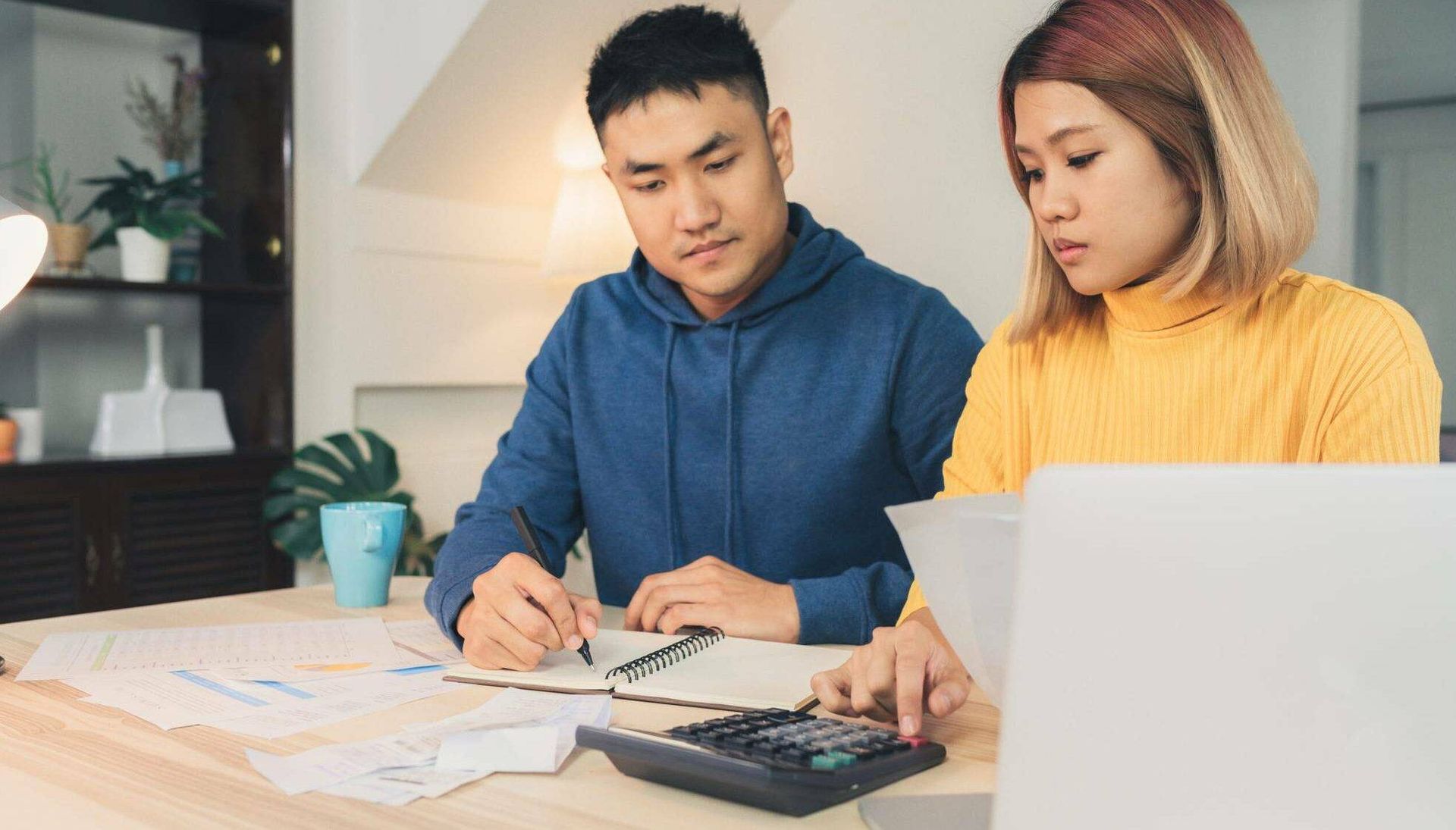 Rewire, bills, guilt, Young couple managing finances, reviewing their bank accounts using laptop computer and calculator at modern home. Woman and man doing paperwork together, paying taxes online on notebook pc.